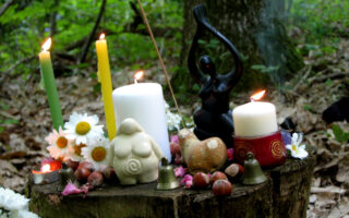 autel en forêt avec statuette de déesses, bougies et fleurs