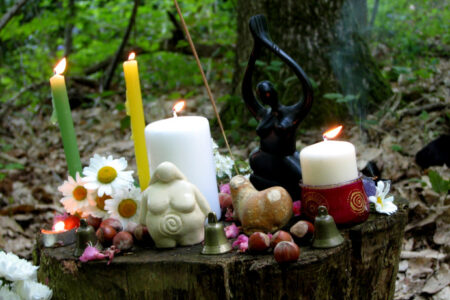 autel en forêt avec statuette de déesses, bougies et fleurs